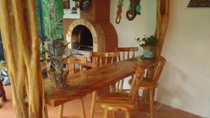 A rustic dining area with a wooden table and chairs, a brick oven, and potted plants. - Casa Lima Bed & Breakfast (San José)