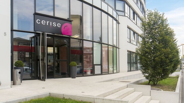 A modern building with a glass facade, a visible entrance, and a small grassy area in front. - Cerise Strasbourg (Strasbourg)
