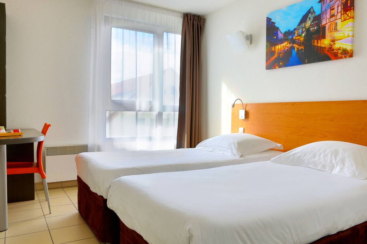 Une chambre d’hôtel avec deux lits, un bureau et une chaise.