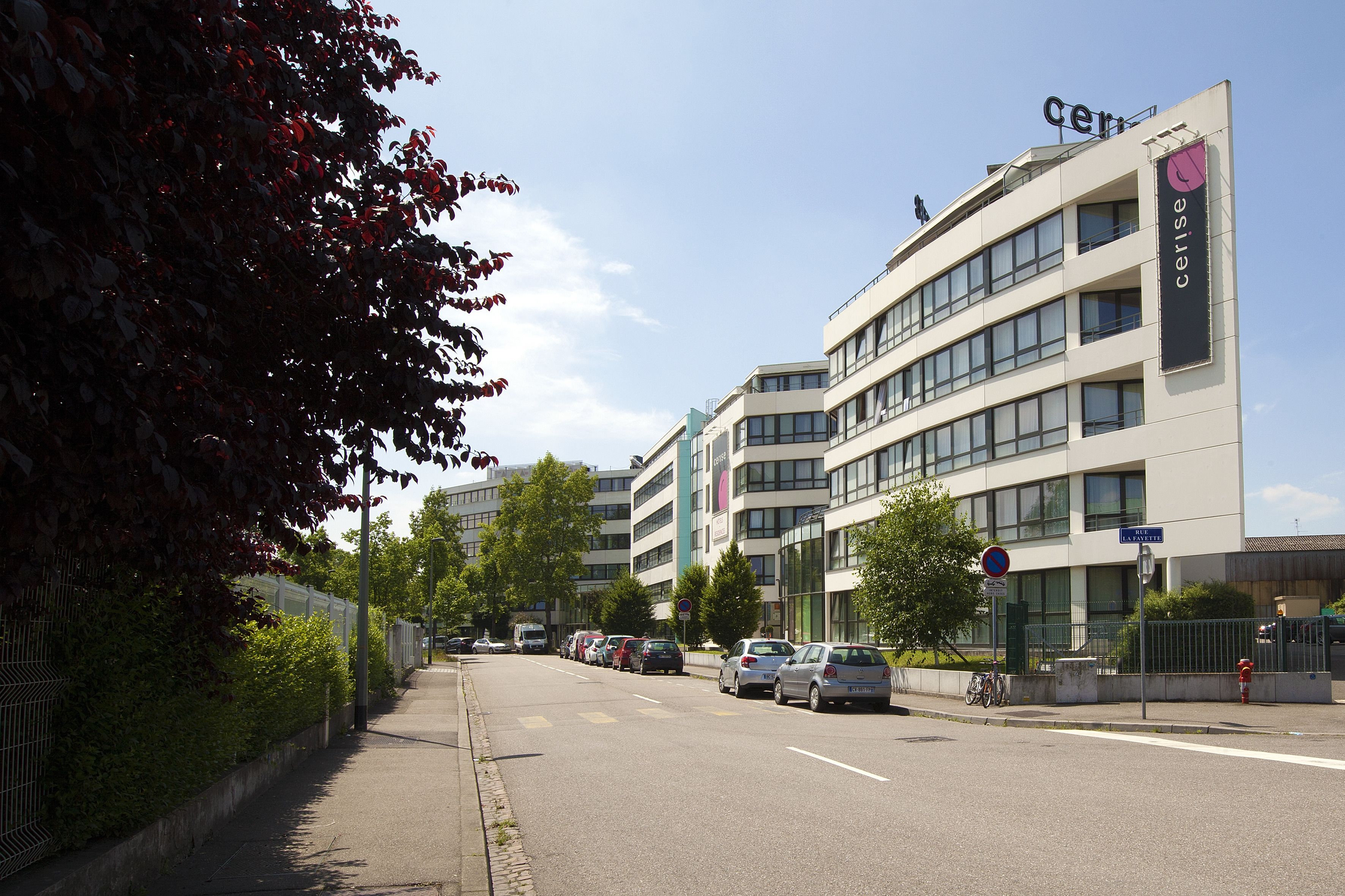 Ein modernes Gebäude mit mehreren Stockwerken, einem Parkplatz und blauem Himmel.