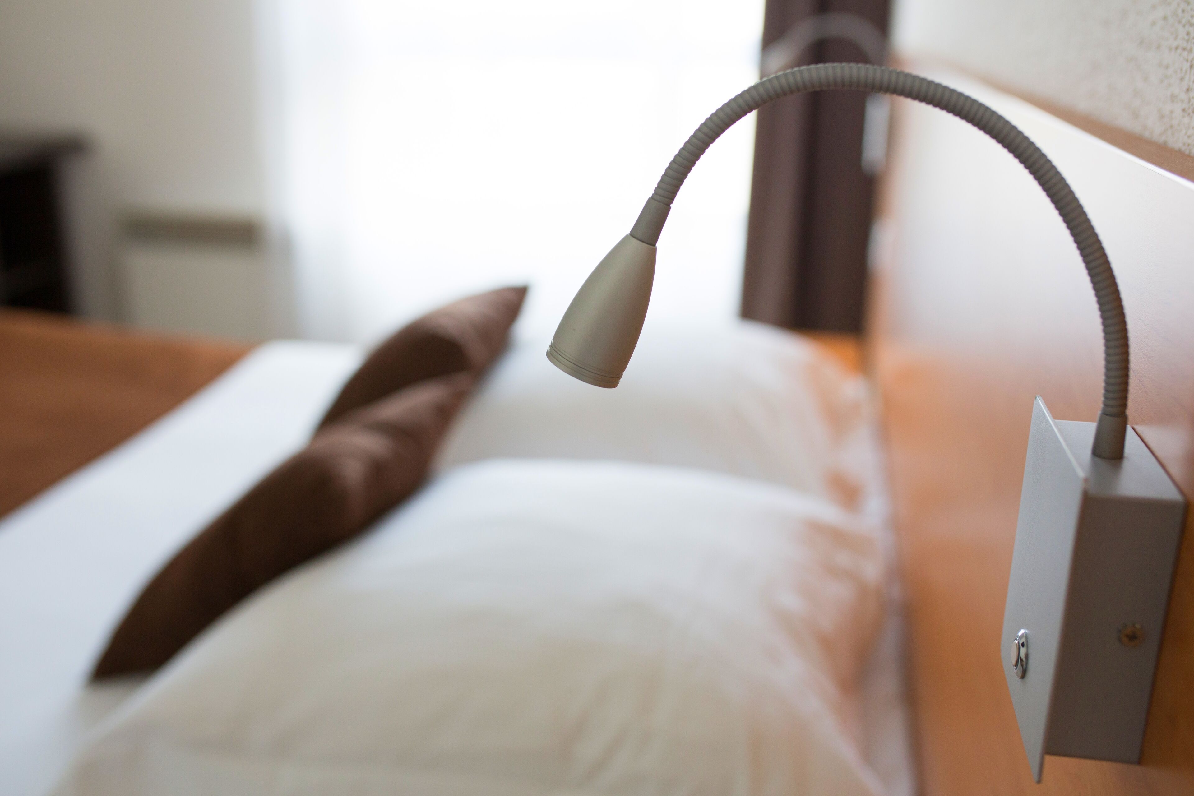 A bed with a white pillow and a brown pillow, a bedside table, and a wall-mounted lamp.
