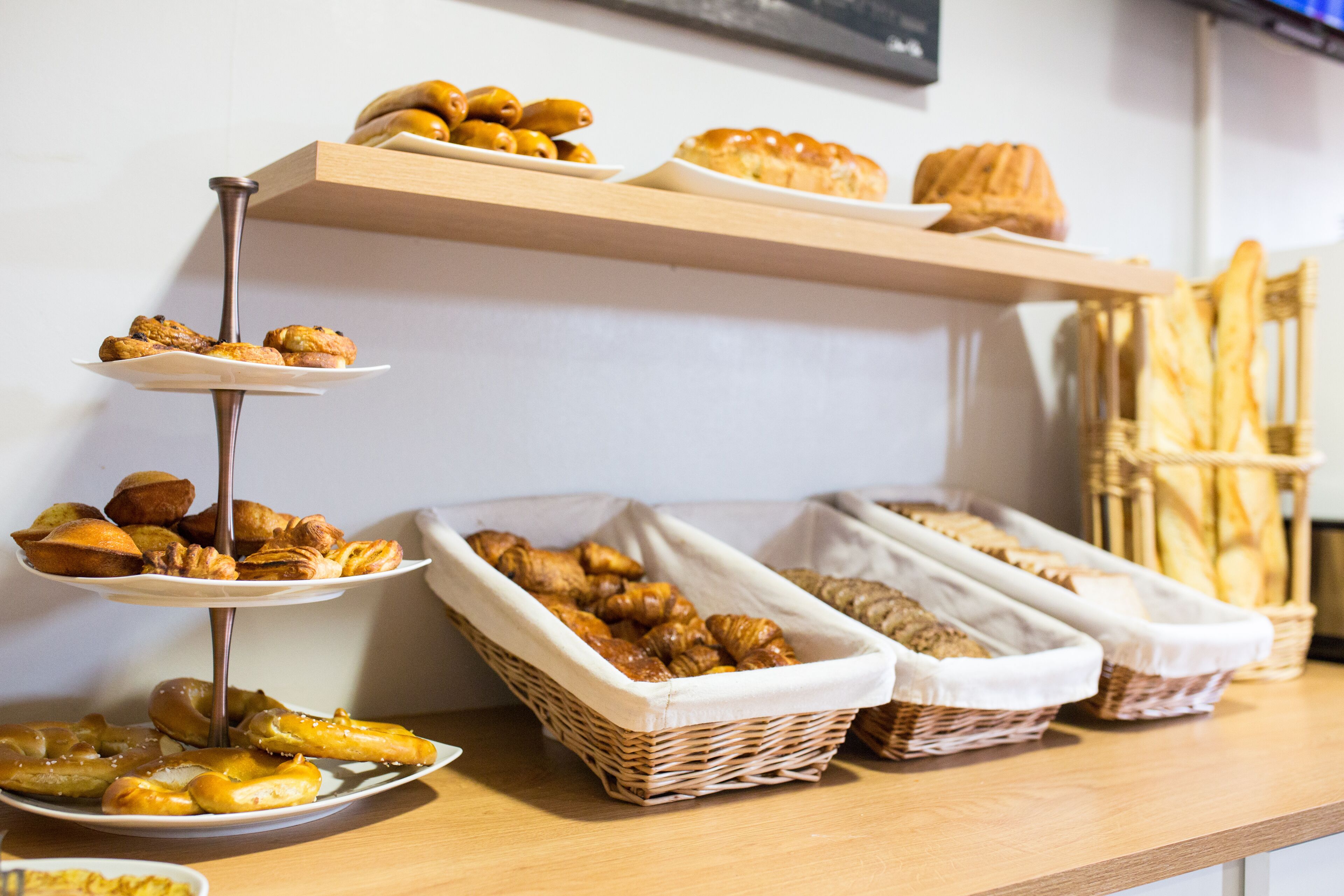 Una mesa de buffet con diversos productos de panadería, como pasteles y pan, dispuestos en estantes y cestas.