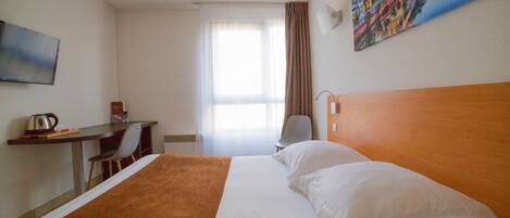A hotel room with a bed, a desk, a chair, and a painting on the wall.