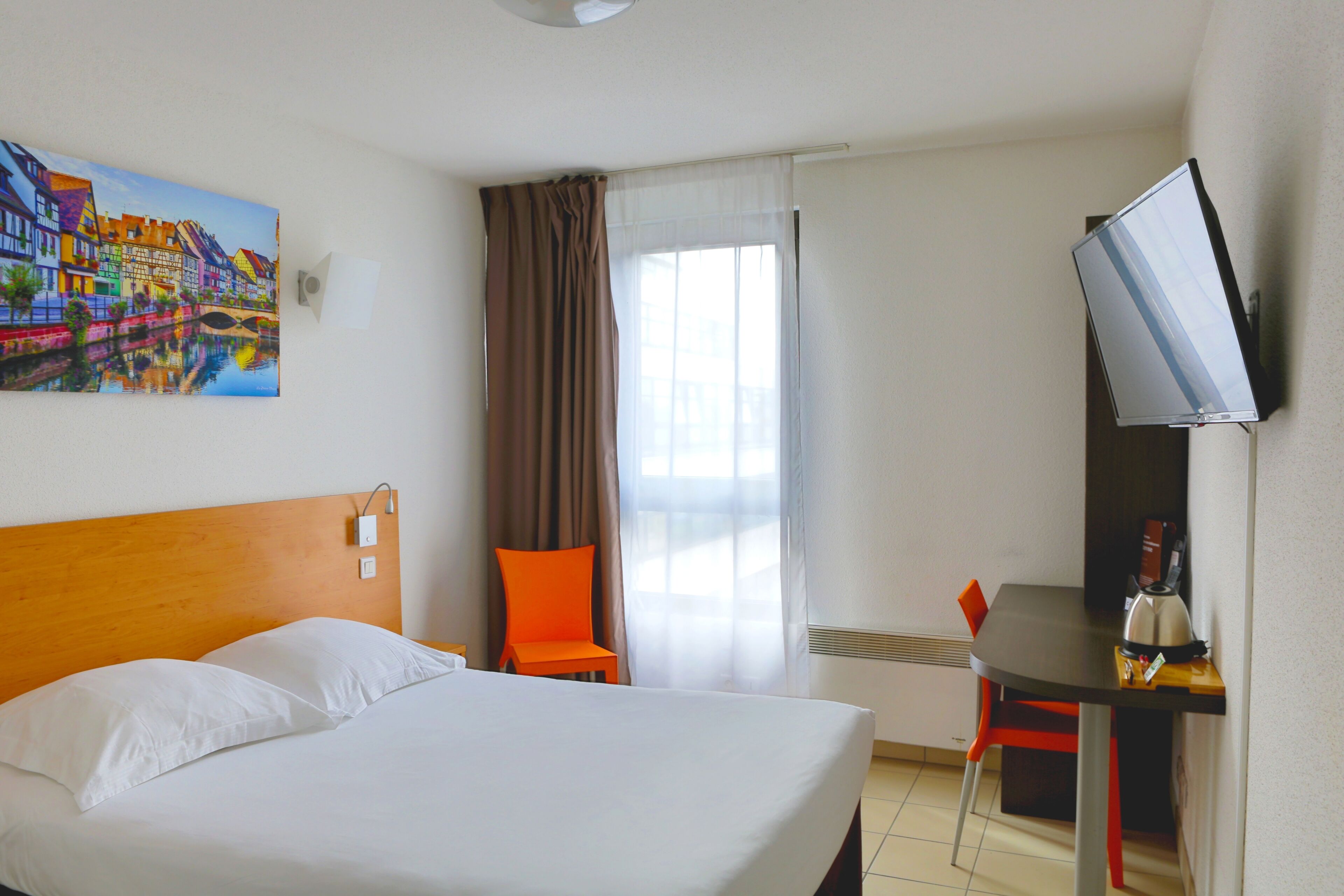 Una habitación de hotel con cama, escritorio con silla, televisión y un cuadro en la pared.