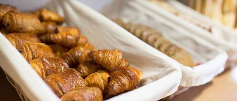 A tray of croissants and a basket of bread on a wooden table.