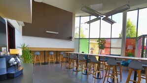 A modern bar area with a coffee machine, bar stools, and large windows offering a view of the outside. - Cerise Strasbourg (Strasbourg)