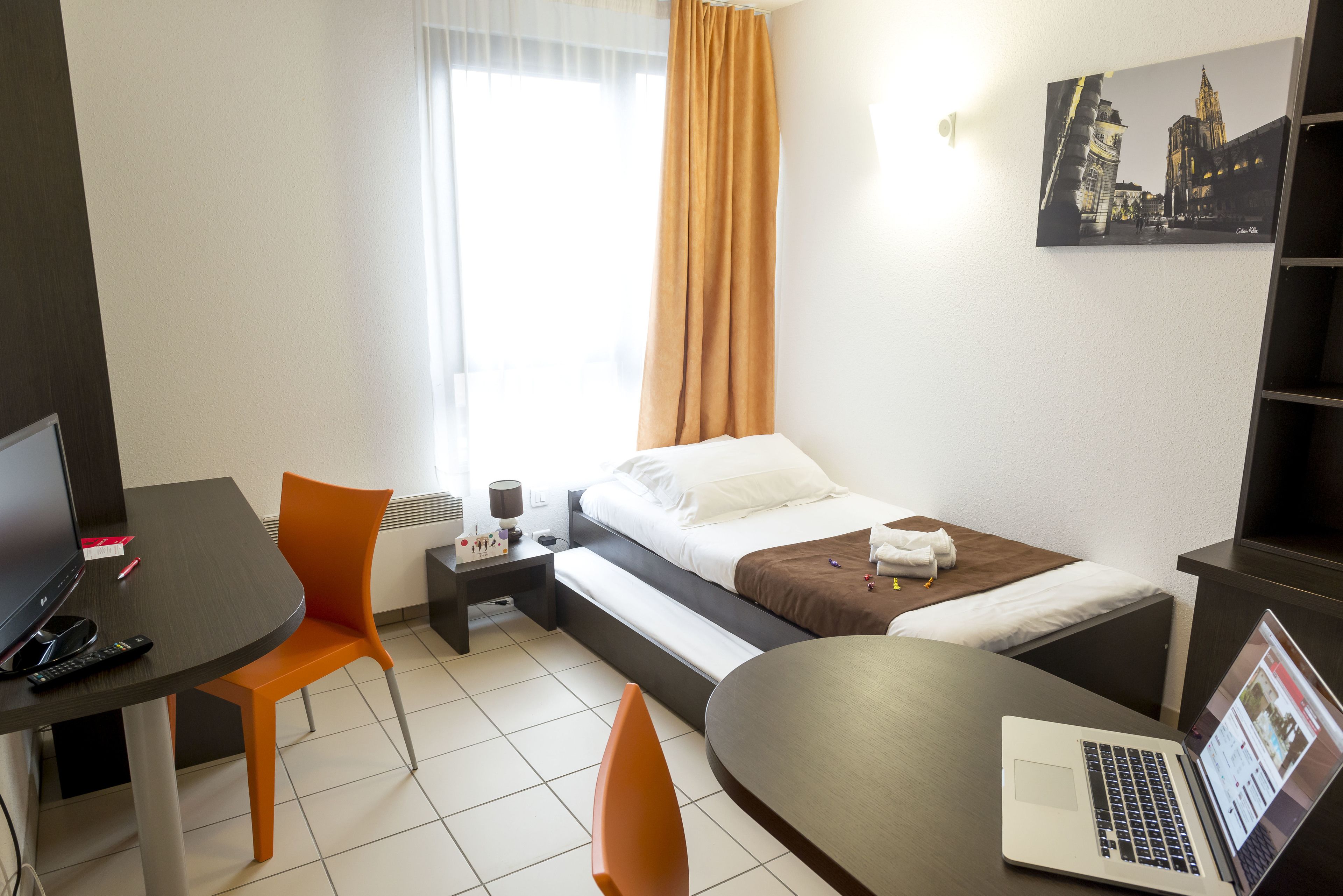 Habitació d'hotel amb un llit, un escriptori amb un ordinador portàtil, una cadira i una televisió.