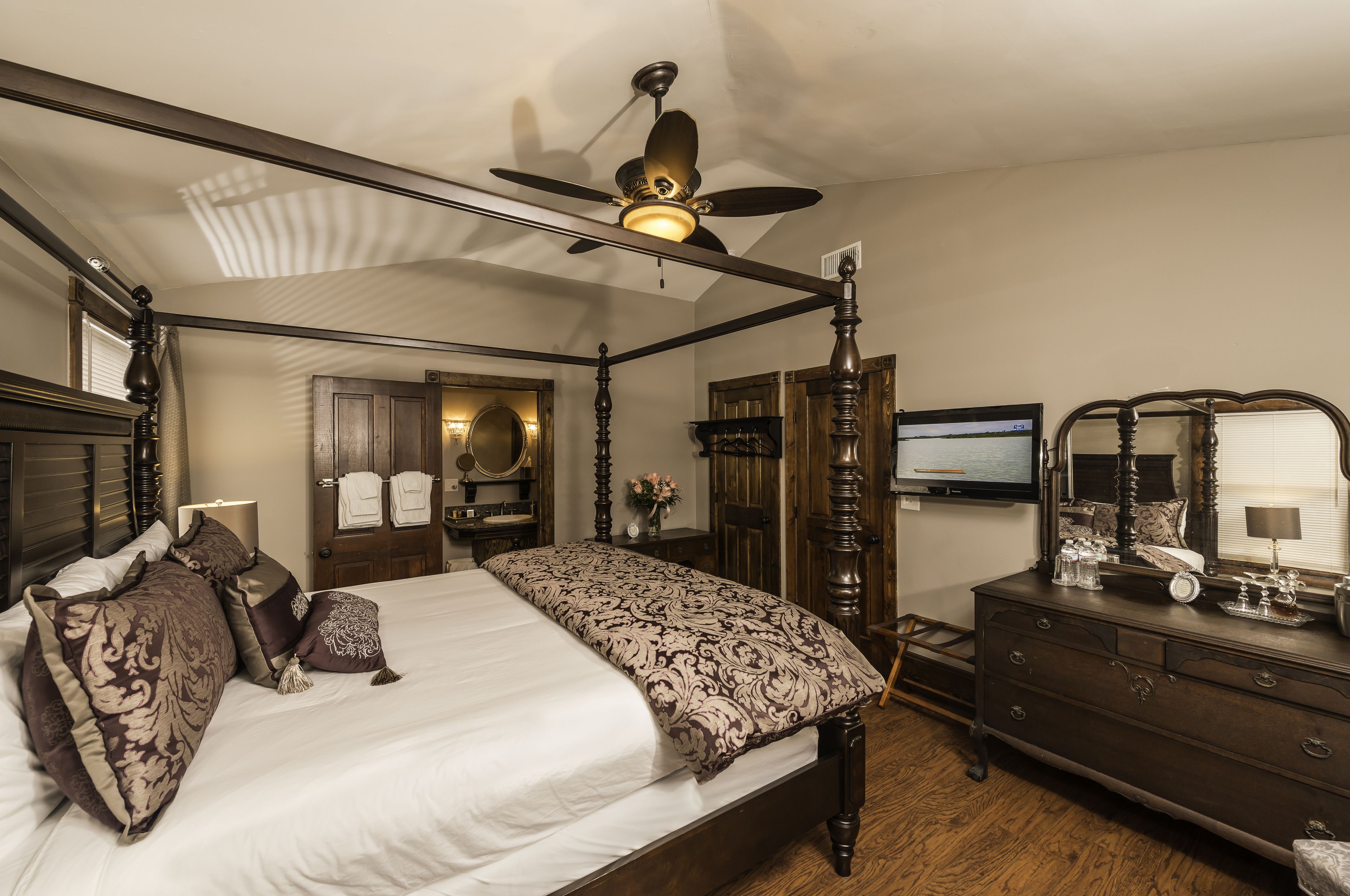 A four-poster bed with a ceiling fan, a dresser with a mirror, and a television on a stand.