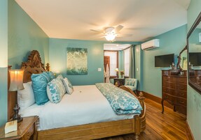 A bedroom with a wooden bed, a ceiling fan, a nightstand, a dresser, and a TV.