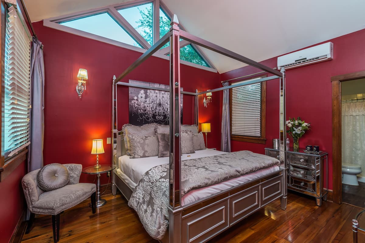 A four-poster bed with a canopy, a bedside table with a lamp, a chair, and a dresser with drawers.