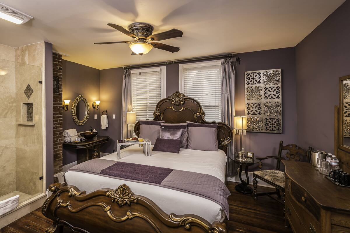 A well-appointed bedroom with a large bed, a vanity with a mirror, a ceiling fan, and a shower area.