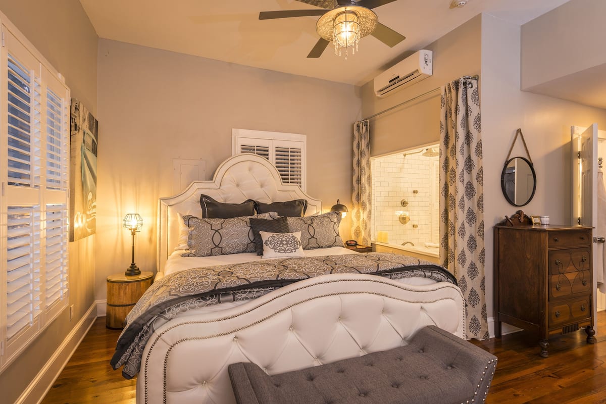 A bedroom with a large bed, a ceiling fan, a window with shutters, and a dresser.