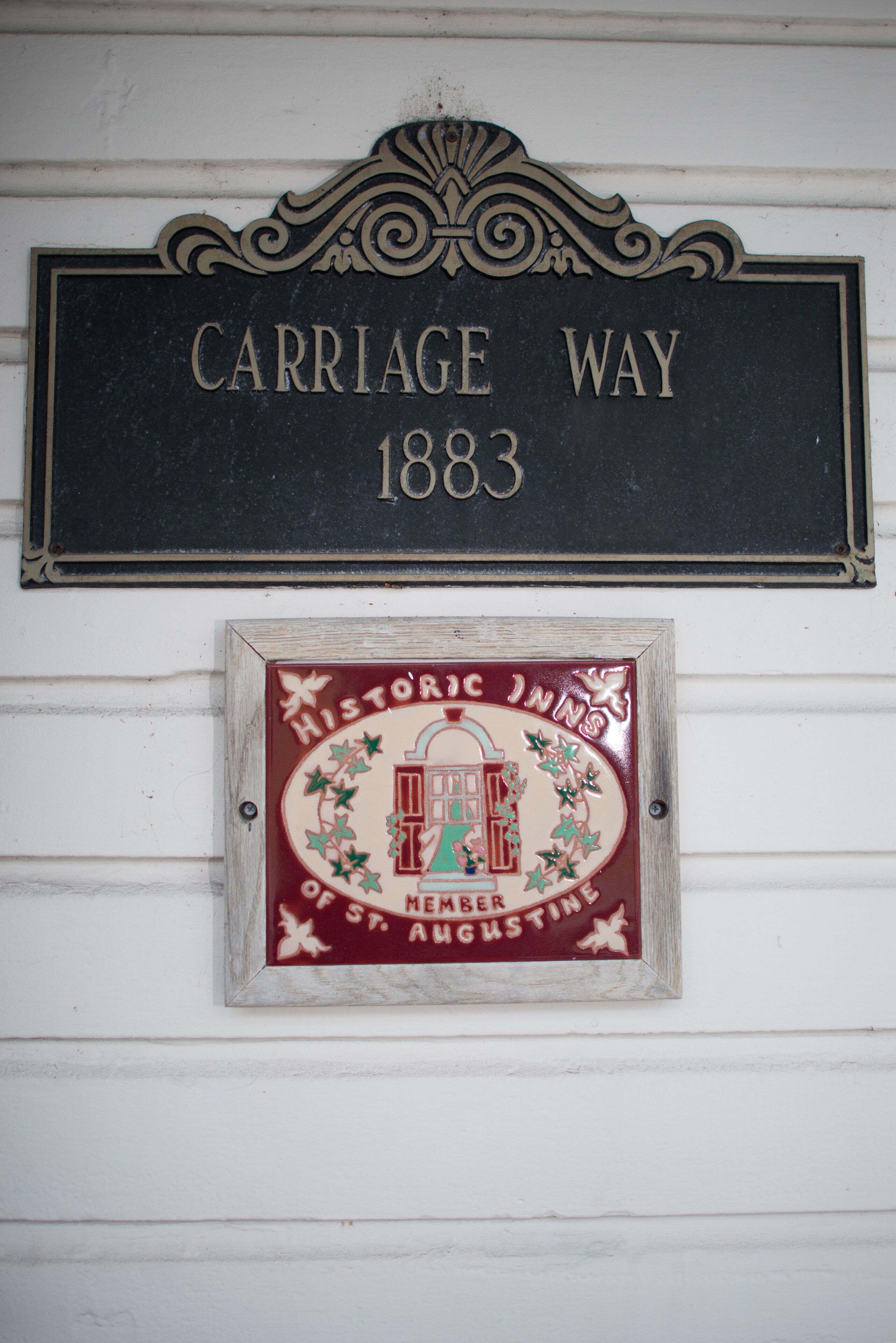 Uma placa preta com a inscrição 'CARRIAGE WAY 1883' e uma placa menor abaixo com a inscrição 'Hotel Histórico de St. Augustine'.