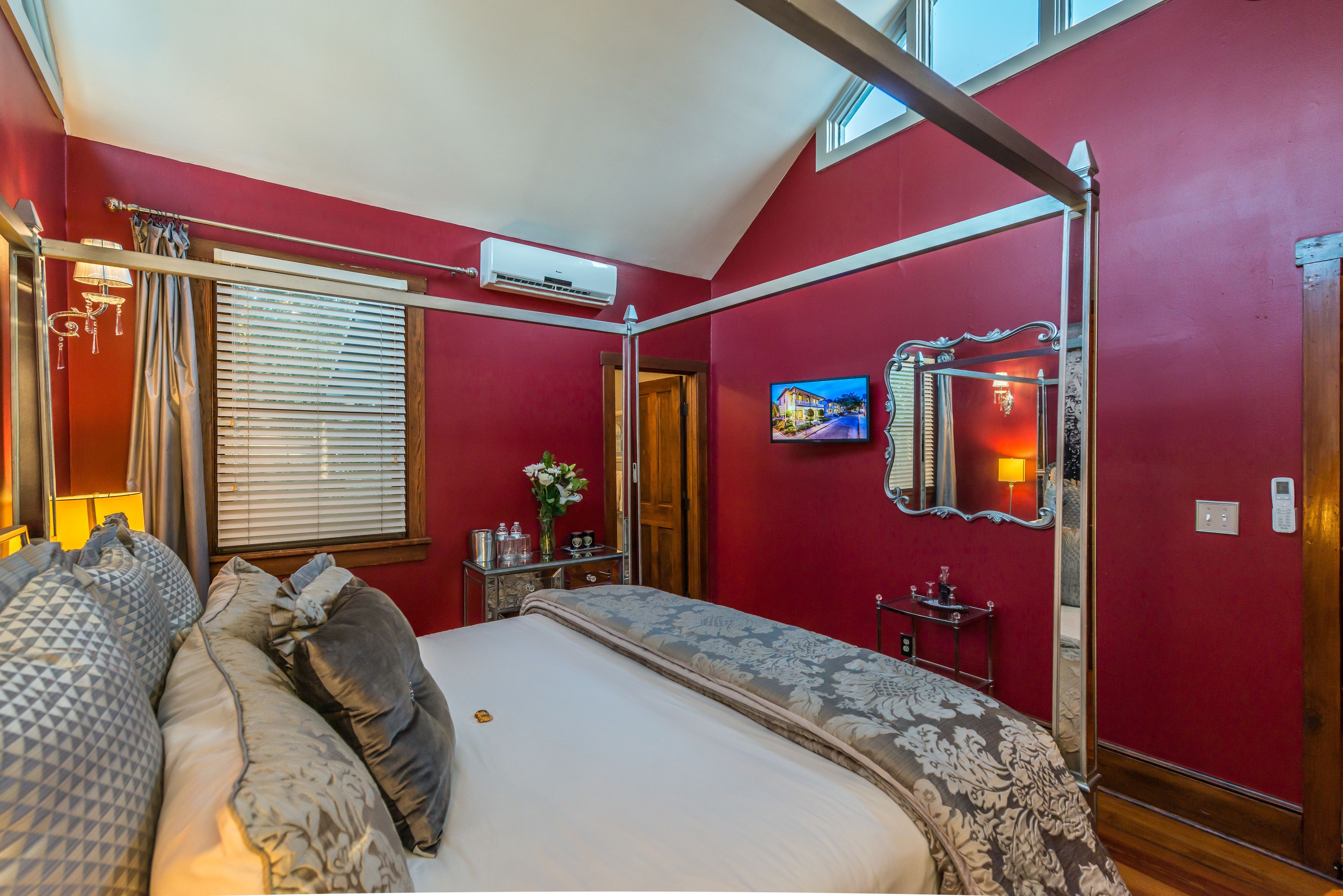 Quarto com cama de dossel, televisão e janela com persianas.