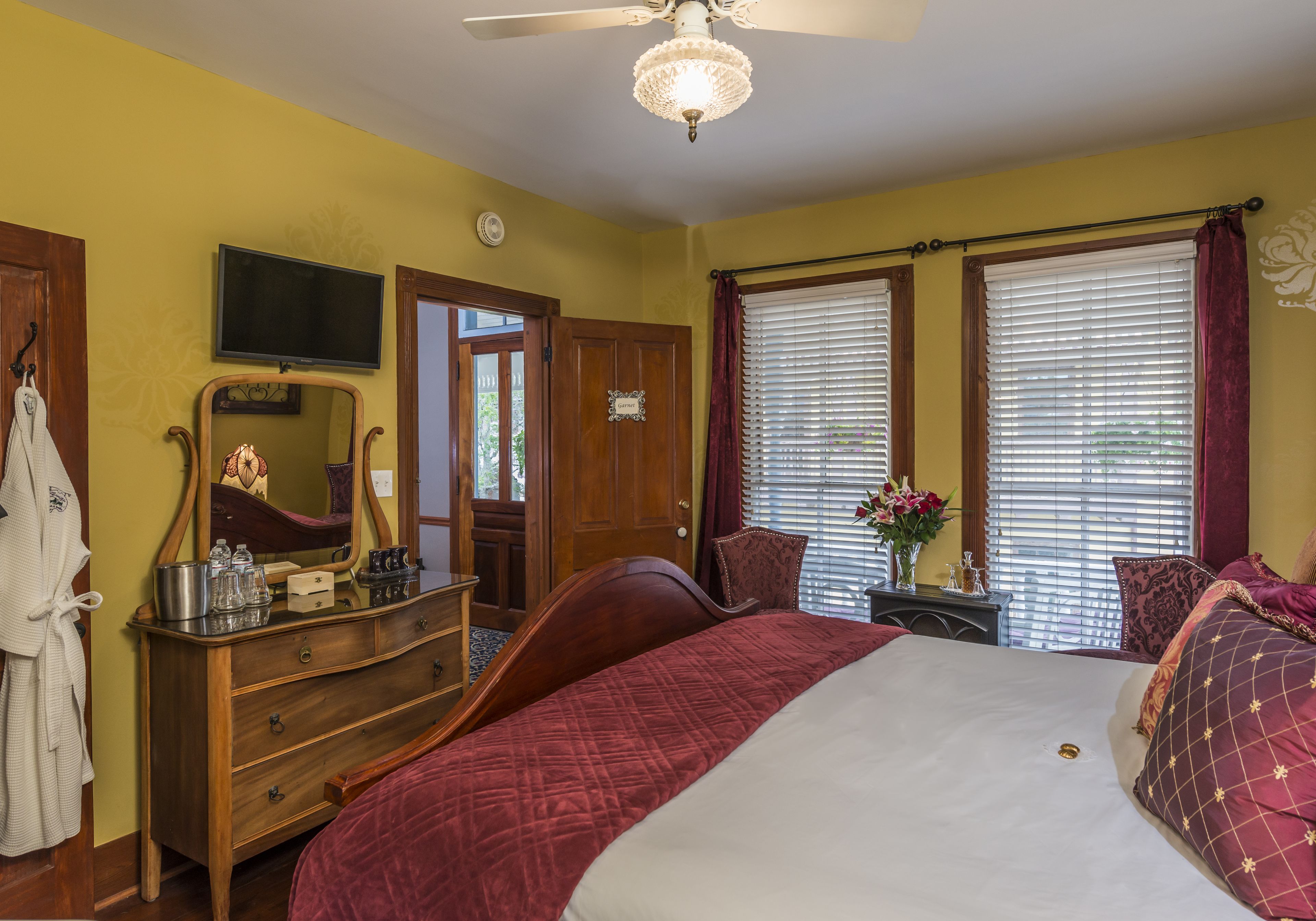 A bedroom with a bed, wooden dresser, vanity, and a ceiling fan.