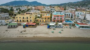 A coastal town with colorful buildings, a beach, and a mountain in the background. - Hotel Rivamare (Ischia)