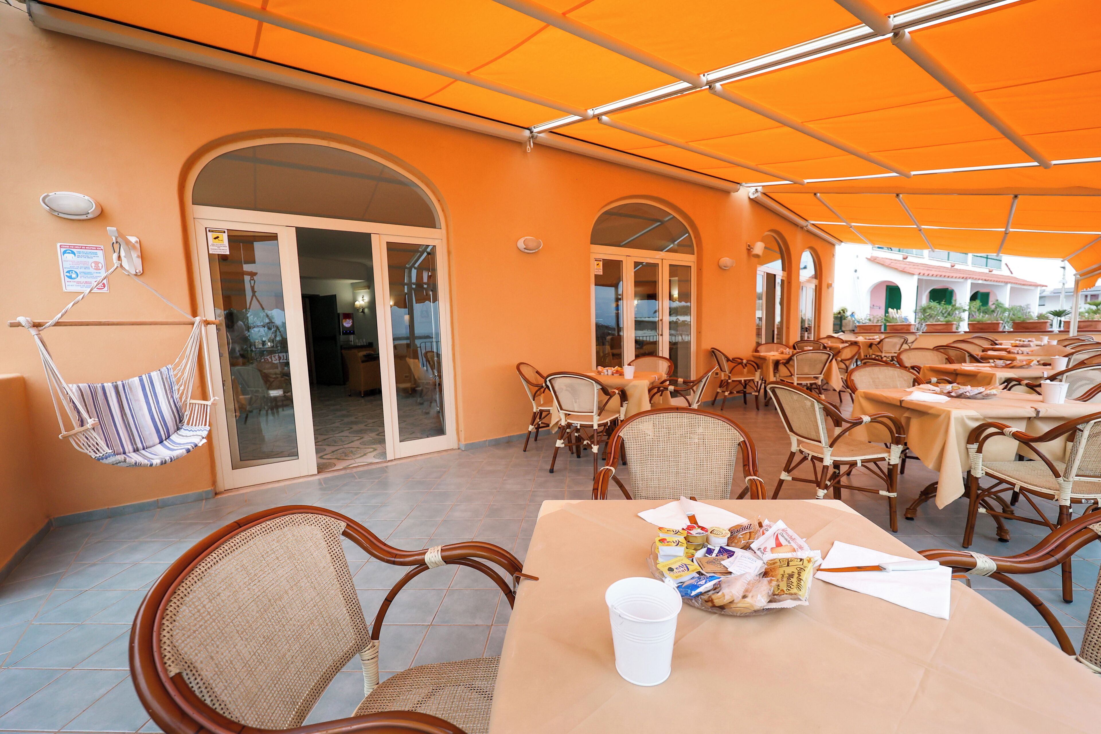An outdoor patio with wicker chairs and tables, covered by a large orange canopy.