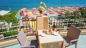 A terrace with a table set for two, overlooking a beach with umbrellas and lounge chairs. - Hotel Rivamare (Ischia)