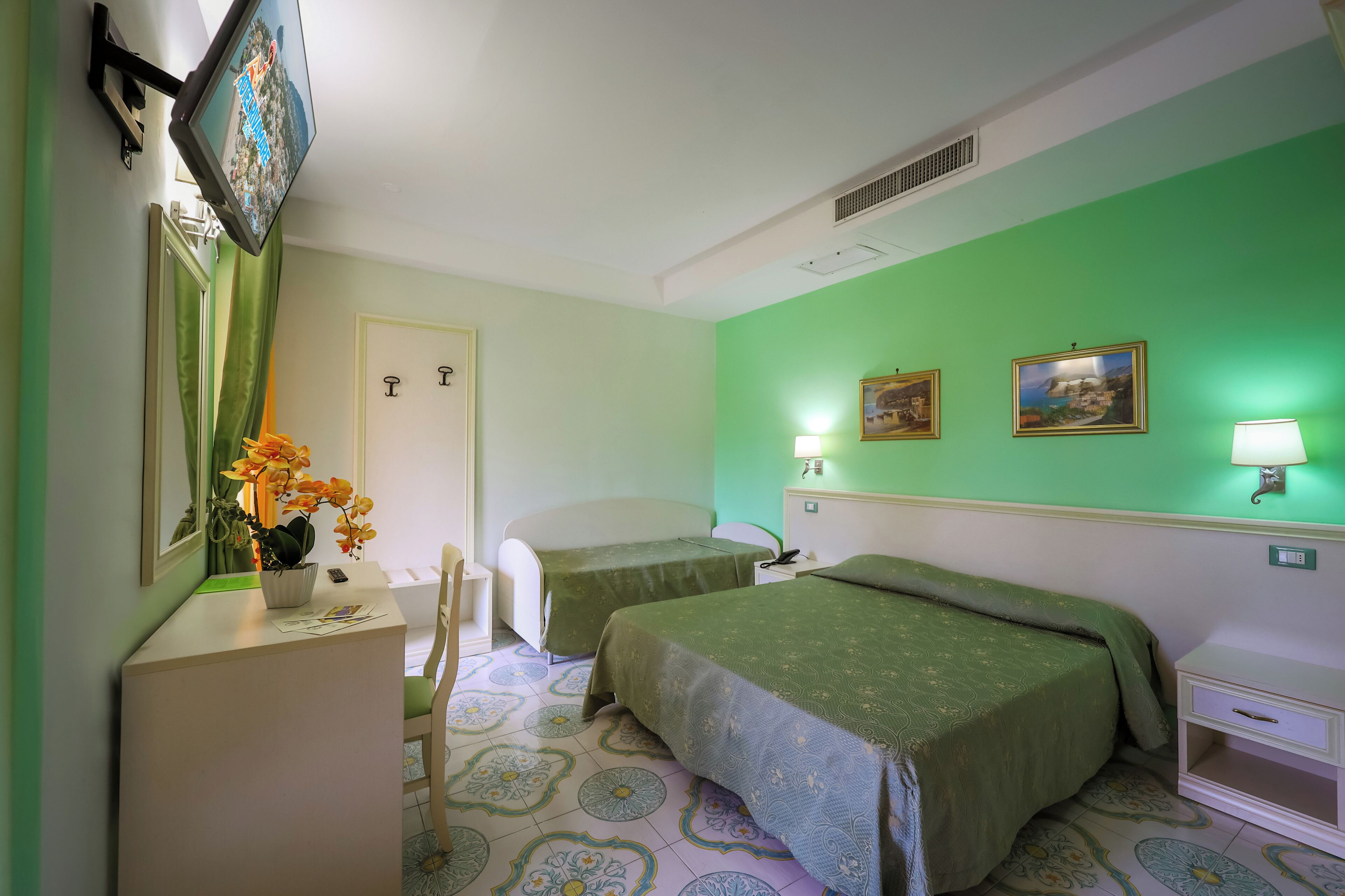 A hotel room with two beds, a desk, a chair, a small table, a mirror, and two wall-mounted lamps.