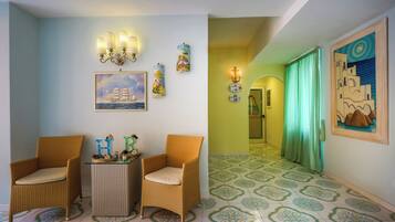 A room with two wicker chairs, a small table, and a wall with nautical-themed artwork.