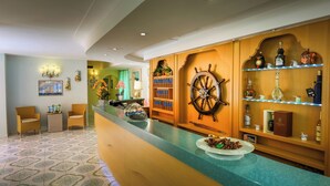 A hotel reception area with a counter, chairs, a ship's wheel decoration, and shelves with bottles. - Hotel Rivamare (Ischia)
