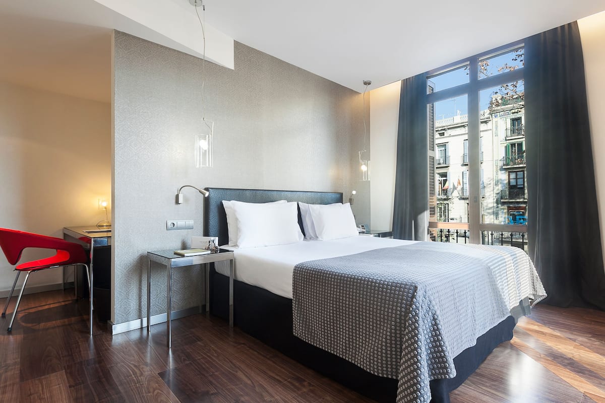 A modern hotel room with a large bed, a desk, and a chair.