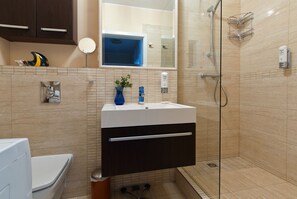 Un baño moderno con ducha envuelta en cristal, un lavabo blanco con un florero azul y un espejo sobre el lavabo.
