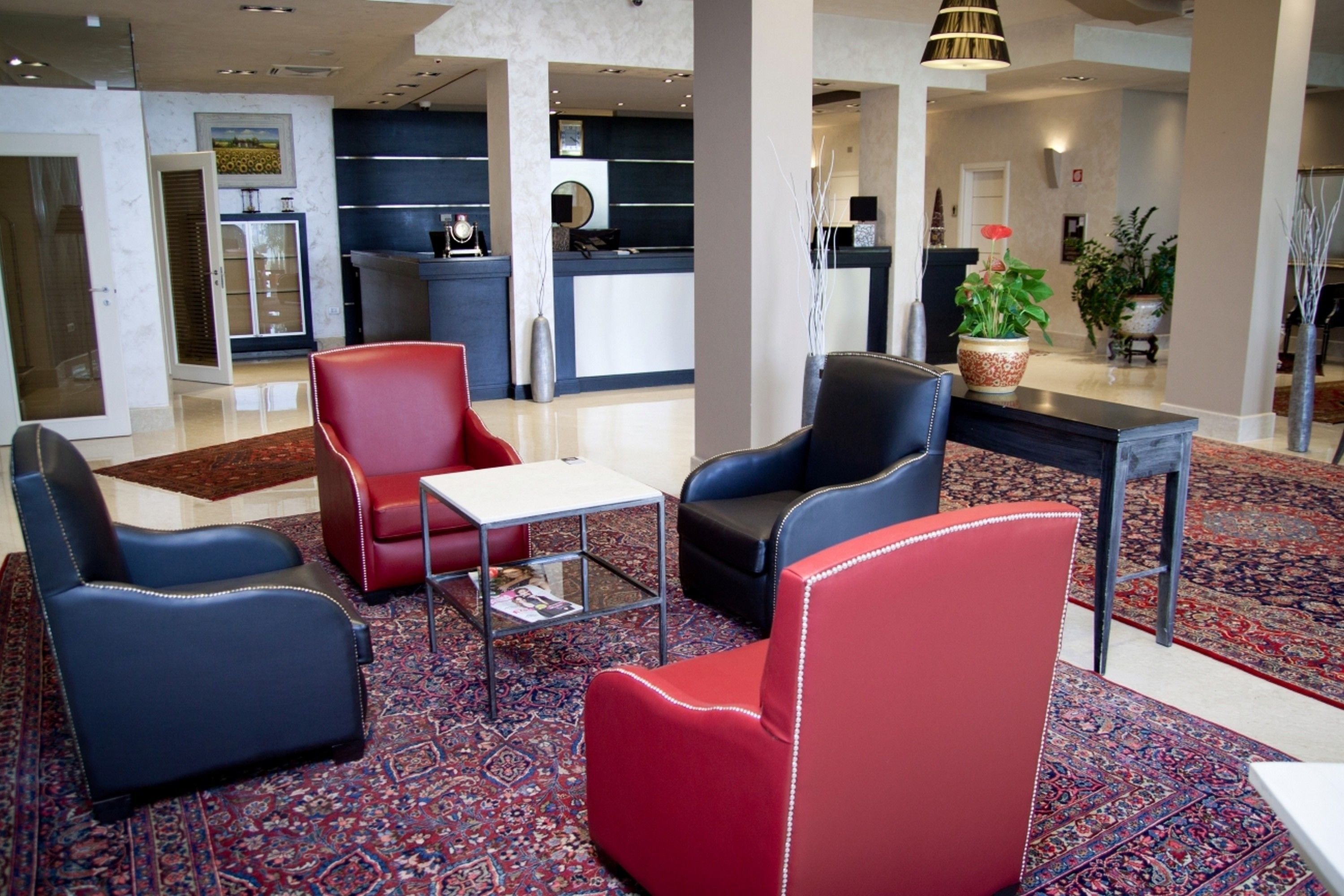 A modern lobby with a reception desk, seating area with red and blue chairs, and a patterned carpet.