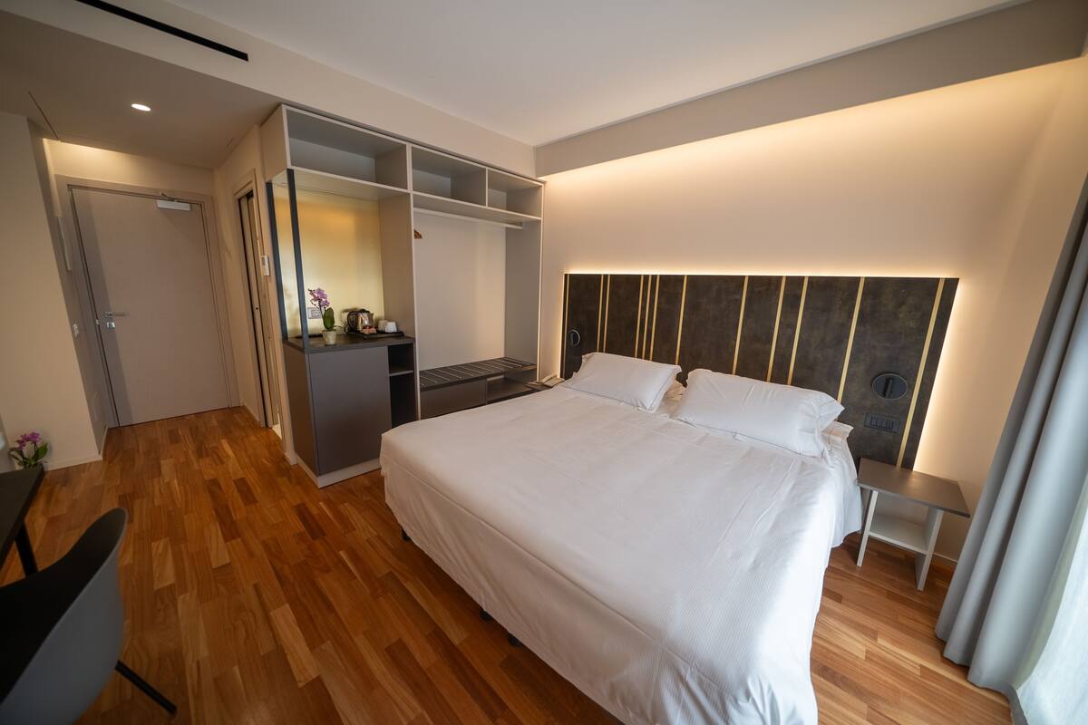 Ein modernes Hotelzimmer mit einem großen Bett, einem eingebauten Kleiderschrank und einer kleinen Schreibtischzeile.