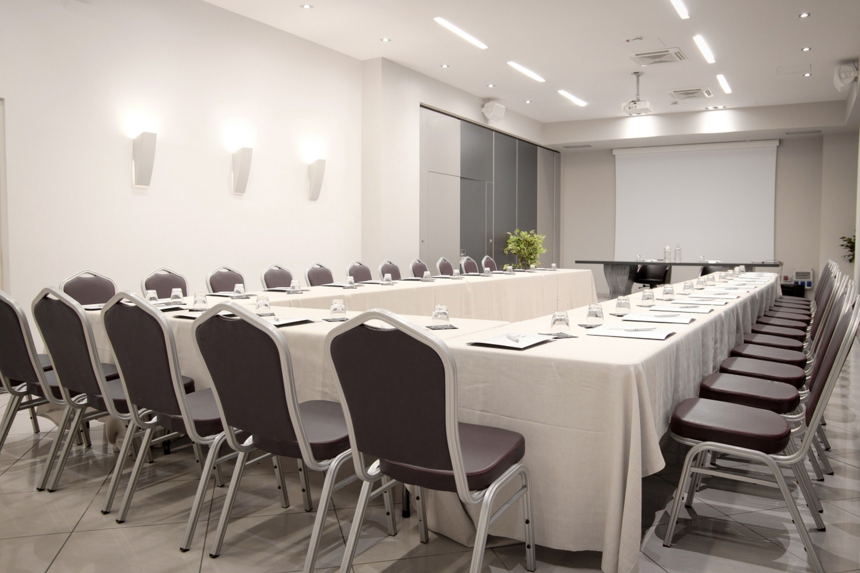 A conference room with a long table, chairs, a projector screen, and a whiteboard.