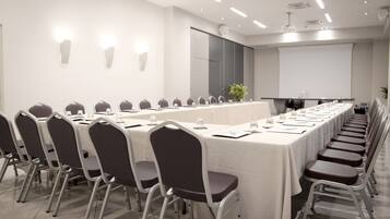 A conference room with a long table, chairs, a projector screen, and a whiteboard.