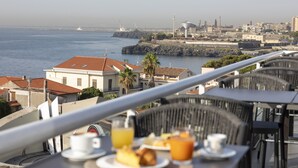 Une terrasse où l’on sert le petit-déjeuner, offrant une vue sur le paysage urbain de la côte, avec ses bâtiments et son port.
