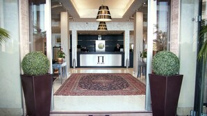 Un hall d’hôtel comprenant un comptoir d’accueil, un grand tapis et deux plantes en pot.