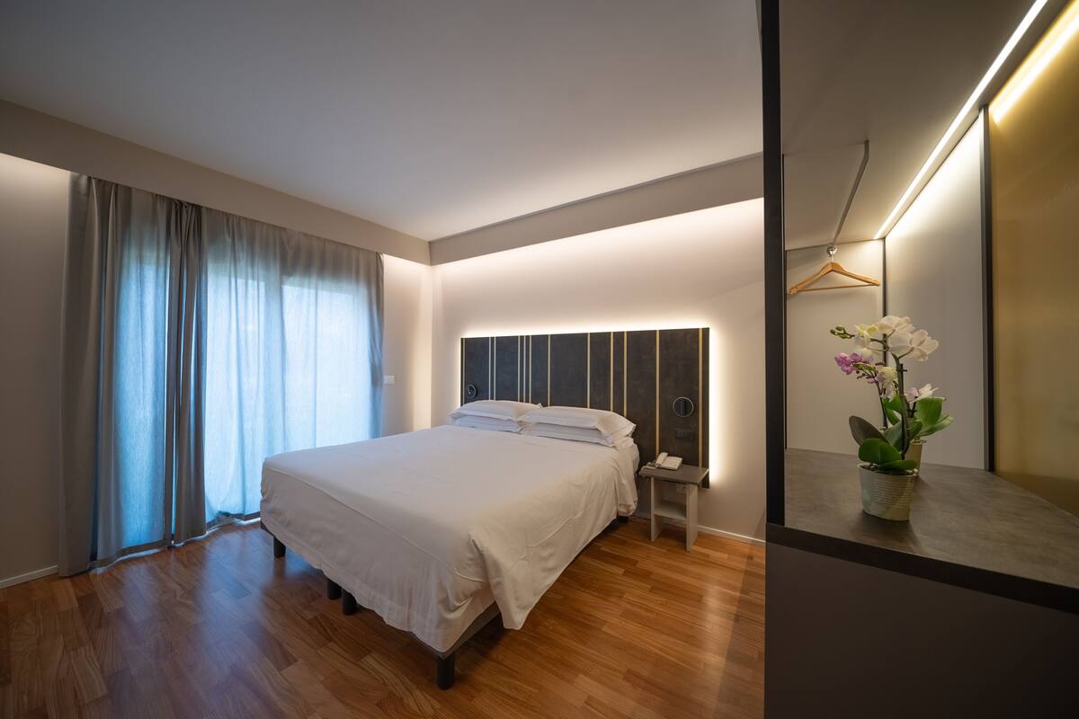 Ein modernes Schlafzimmer mit einem großen Bett, Nachttischen, einem Beistelltisch und einem Spiegel mit Pendelleuchte.