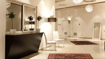 Un moderno vestíbulo de hotel con una recepción, sillas blancas, un espejo grande e iluminación decorativa.