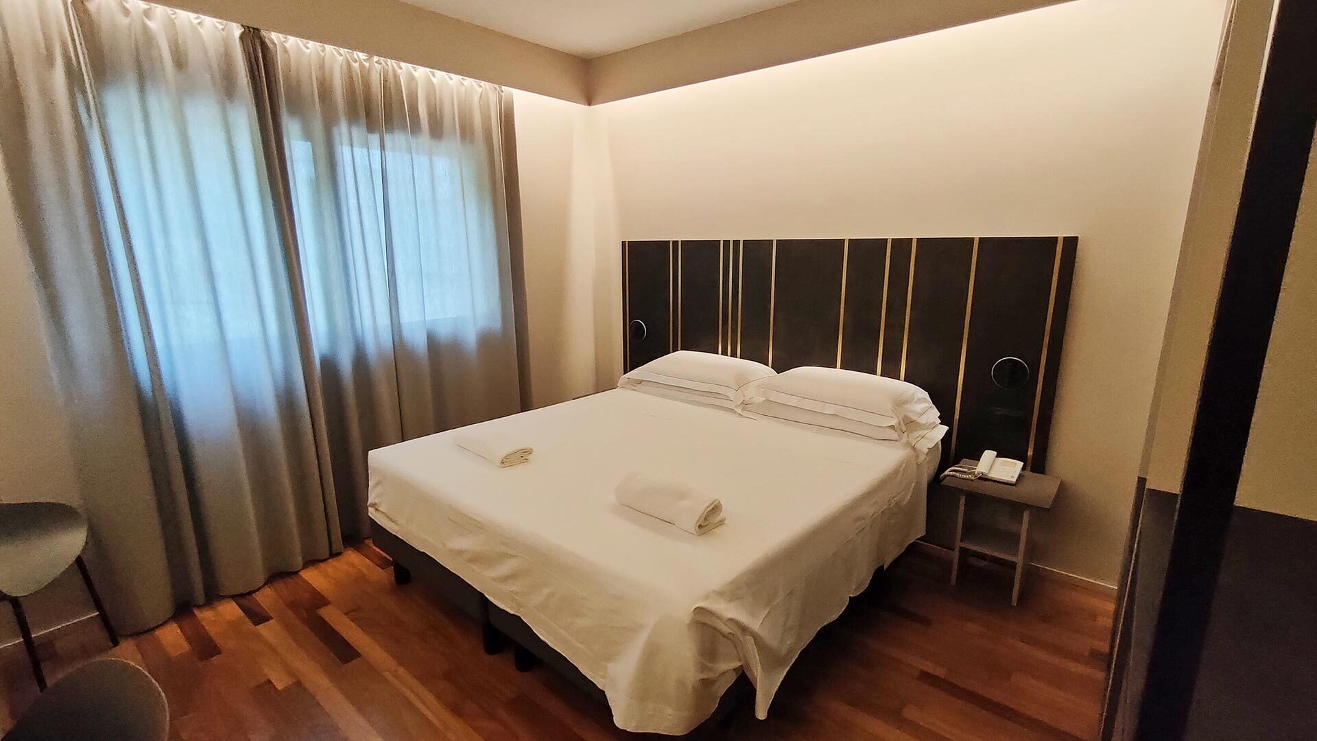 Une chambre d’hôtel avec un lit, des rideaux, une table de chevet avec un téléphone et une chaise.