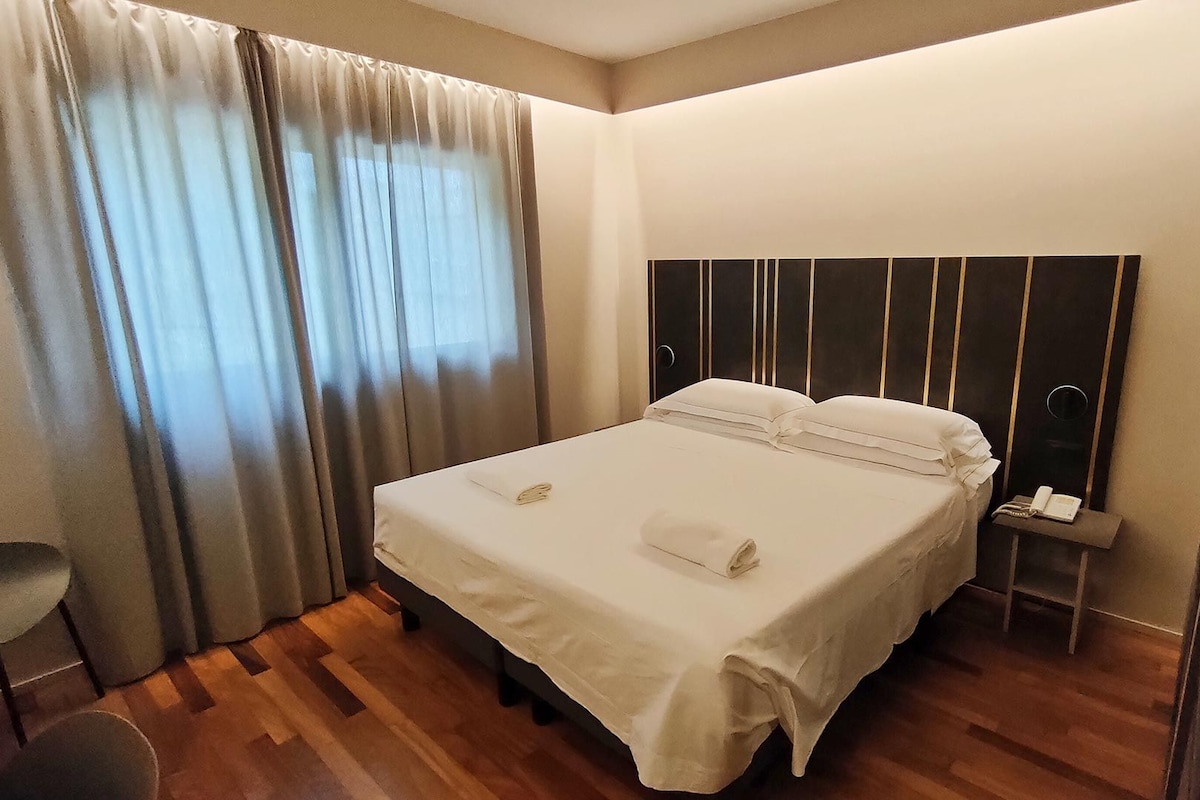 Une chambre d’hôtel avec un lit, des rideaux, une table de chevet avec un téléphone et une chaise.