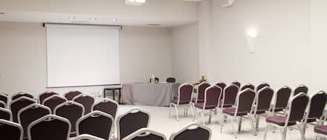 A conference room with rows of chairs, a projector screen, and a table with a tablecloth.