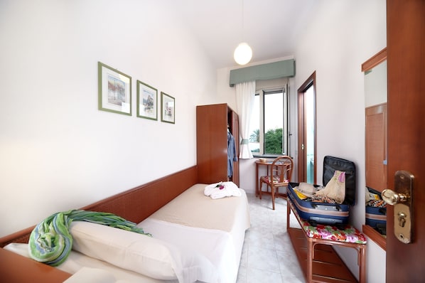A hotel room with a bed, a desk, a chair, a suitcase, and a window. - Hotel Ulisse (Ischia)