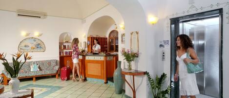 Un vestíbulo de hotel con una recepción, un sofá, un jarrón grande y un ascensor.