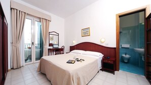 Una habitación de hotel con cama, mesita de noche y baño con lavabo e inodoro.