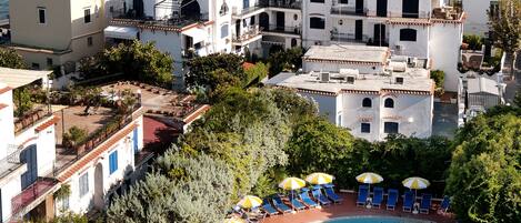 A coastal town with a historic castle, a swimming pool with sun umbrellas, and a marina with boats.
