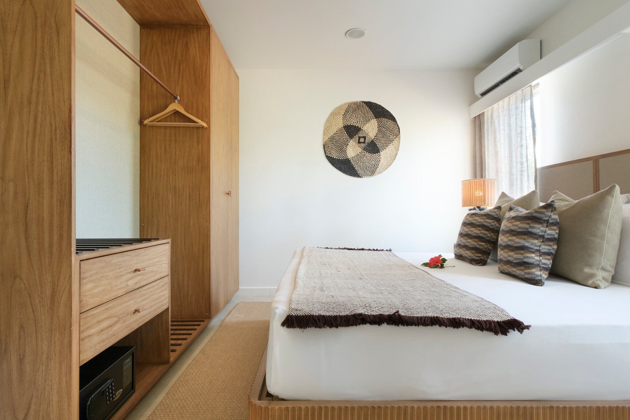 A bedroom with a bed, a wooden wardrobe, a wall-mounted circular artwork, and a bedside lamp.