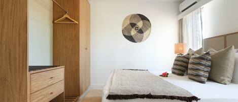 A bedroom with a bed, a wooden wardrobe, a wall-mounted circular artwork, and a bedside lamp.