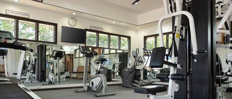 Un gimnasio con equipo de ejercicio, ventanas amplias y un reloj en la pared.