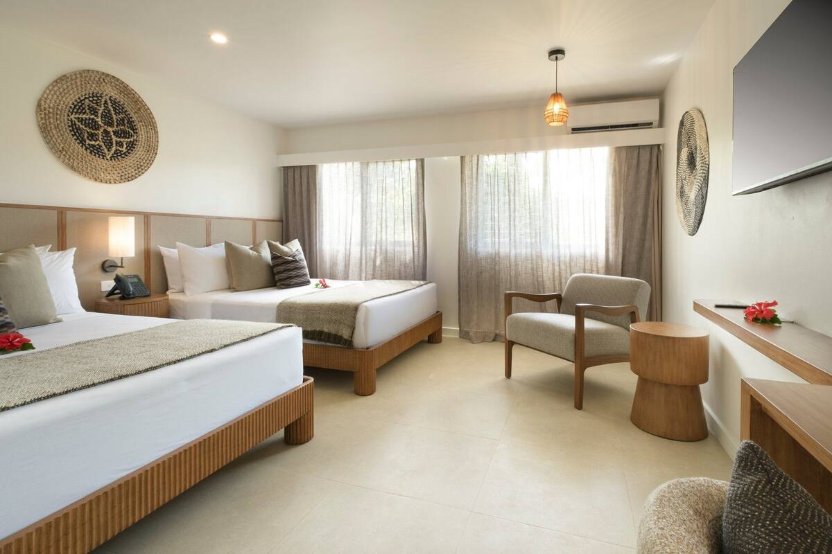 A hotel room with two beds, a chair, a small table, and a TV.