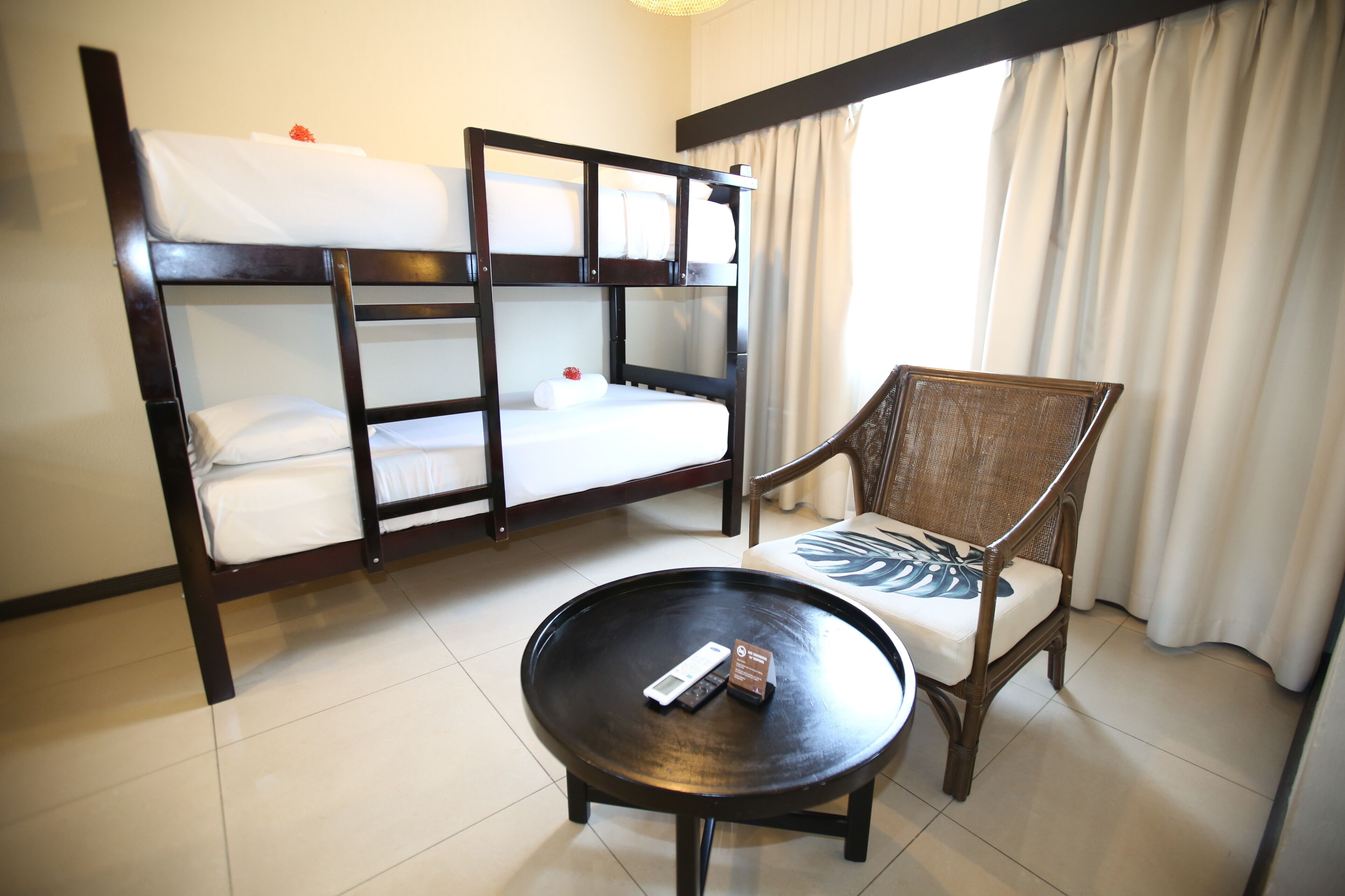 Quarto de hotel com beliches, uma mesa redonda e uma cadeira.