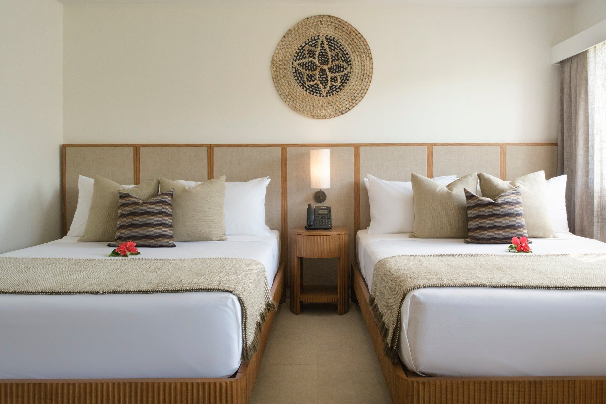 Camera d'albergo con due letti, un comodino con una lampada, un quadro appeso al muro e un piccolo fiore su ciascun letto.