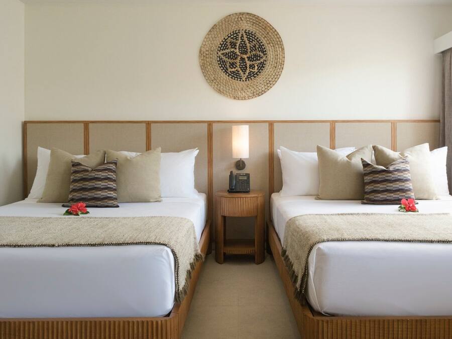 Camera d'albergo con due letti, un comodino con una lampada, un quadro appeso al muro e un piccolo fiore su ciascun letto.