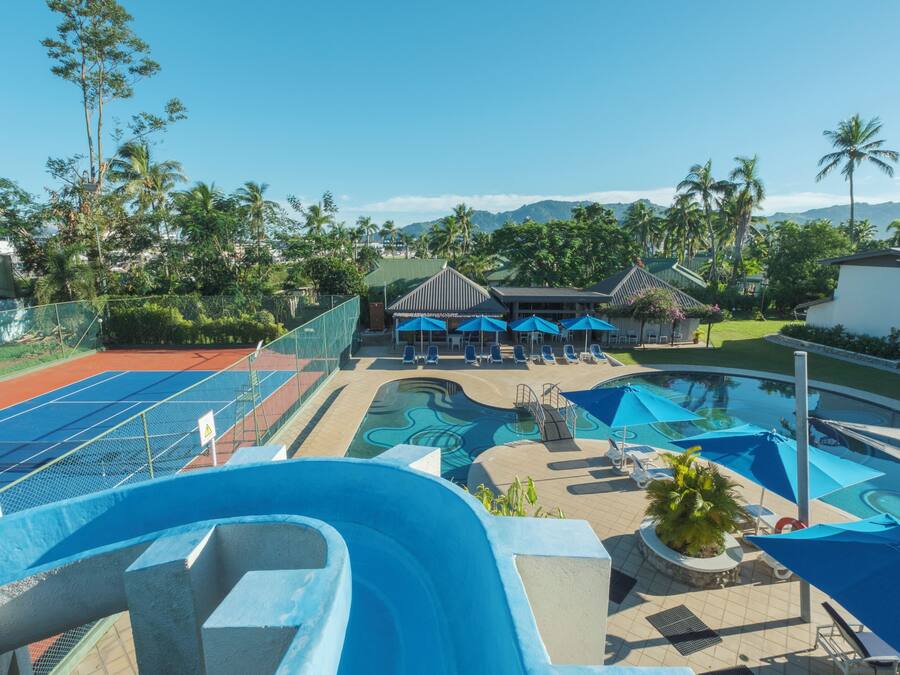 A resort with a swimming pool, sun loungers, and a tennis court.